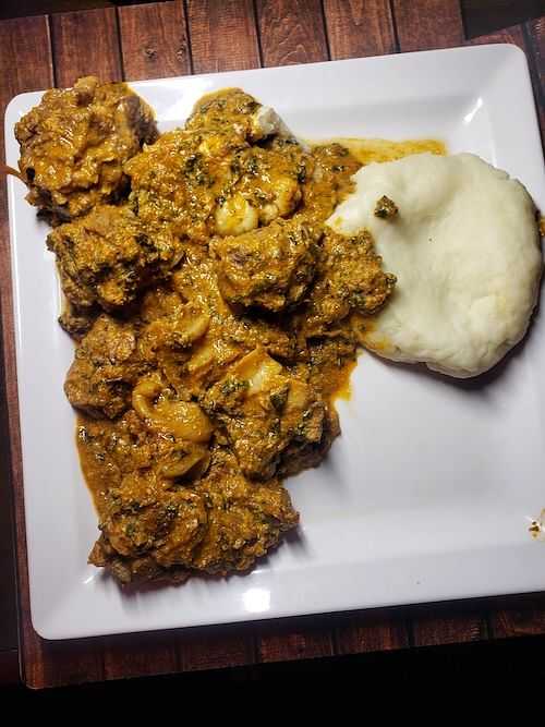 Plate of stew with meat and a side of fufu on a wooden table.